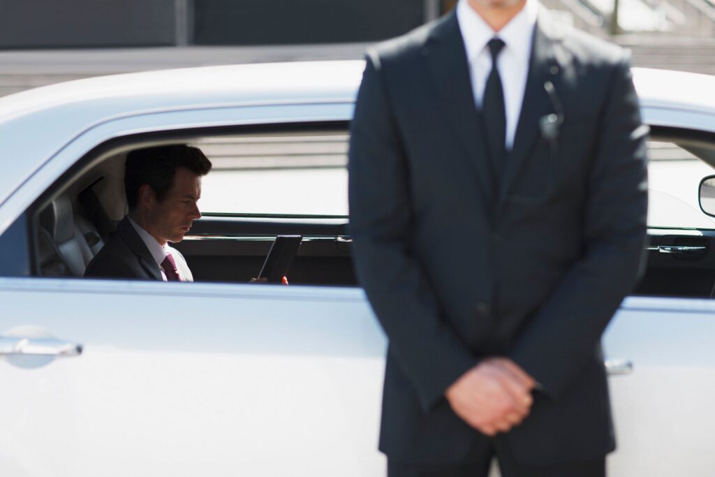 A man in a suit and tie is standing in front of a white car.