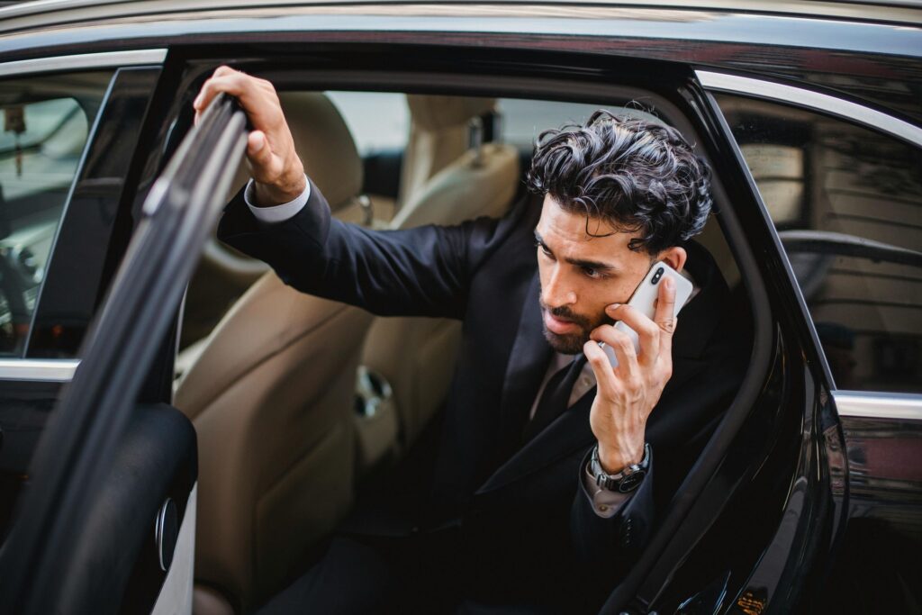 A man in a suit is talking on a cell phone while getting out of a car.